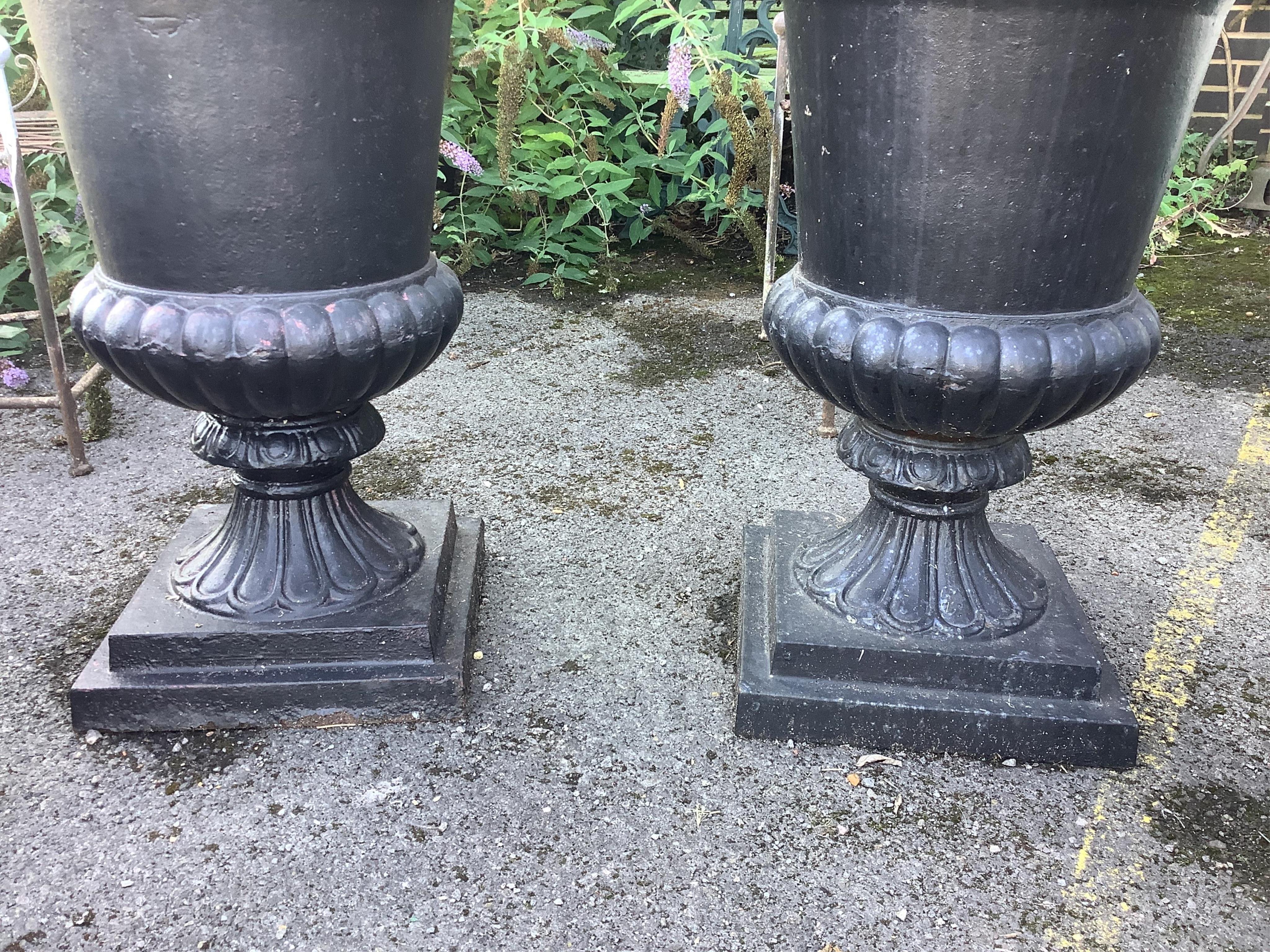 A pair of Victorian style black painted cast iron campana shaped garden urns, on square plinths, diameter 54cm, height 80cm. Condition - fair